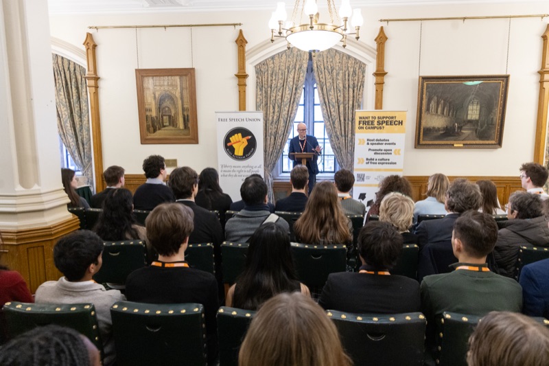 Grant recipients seated in a House of Commons committee room, listening to a speaker at the front beside a Free Speech Union banner